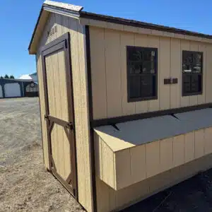 Front and side view of tan chicken coop with brown trim, two windows, and exterior nesting box.