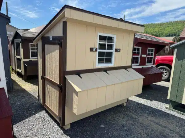 Stoltzfus tan 4x6 leantoo chicken coop with brown trim, single window, and exterior nesting box, set on gravel.