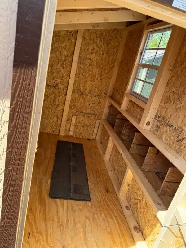 Interior of a 4x6 leantoo chicken coop with unfinished wood, window, nesting boxes, and roosting bars.