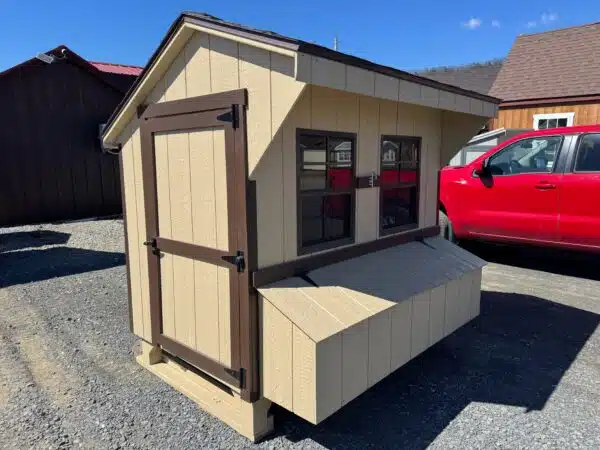 Stoltzfus tan 4x6 leantoo chicken coop with brown trim, single window, and exterior nesting box, set on gravel.
