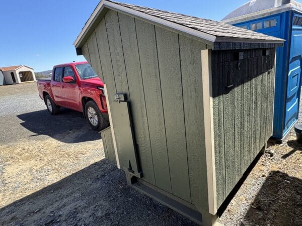 Side angle of a green chicken coop with single door, shown beside a red pickup truck at Wunderbar Structures.
