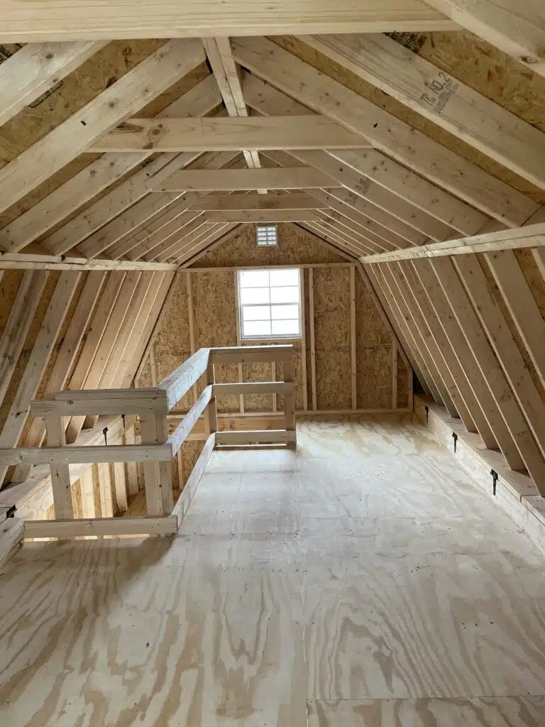Upstairs loft of a new 10x20 two-story barn with unfinished wood framing, window, and safety rail.