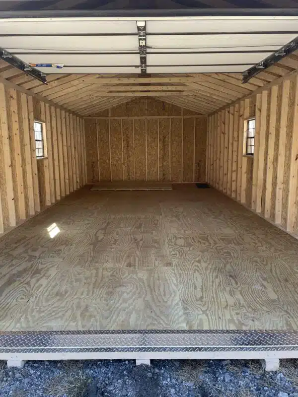 Unfinished interior of a 14x28 A-frame garage with exposed studs, plywood flooring, two side windows, and an open overhead garage door with a metal tread plate at the entrance.