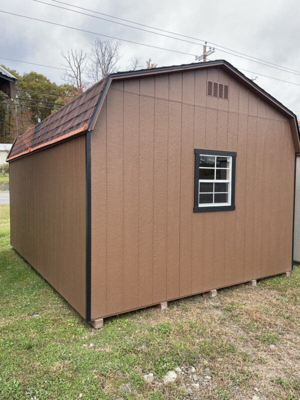 Chestnut brown Dutch barn-style shed with black trim and a single window, set on grass under a cloudy sky.