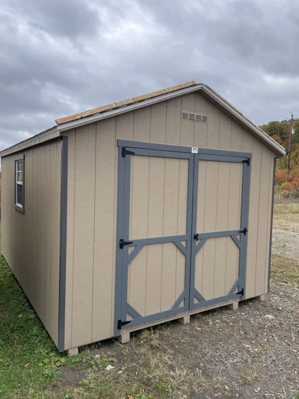 Gap gray Carolina Cottage shed with blue gray trim, charcoal roof, white overhead door, 9-lite entry door, two windows with trim, and a wooden ramp.
