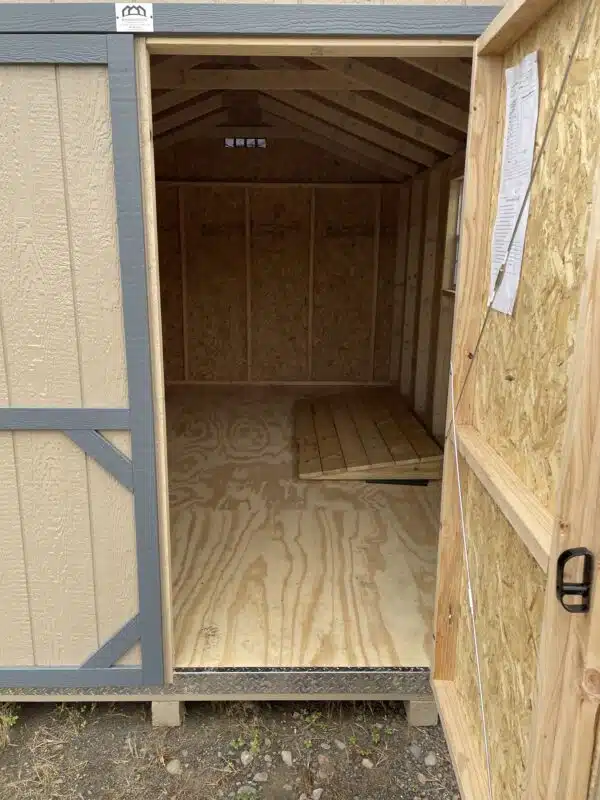 Unfinished interior of a 10x16 Carolina Cottage shed with exposed studs, plywood floor, two side windows, and an overhead garage door.