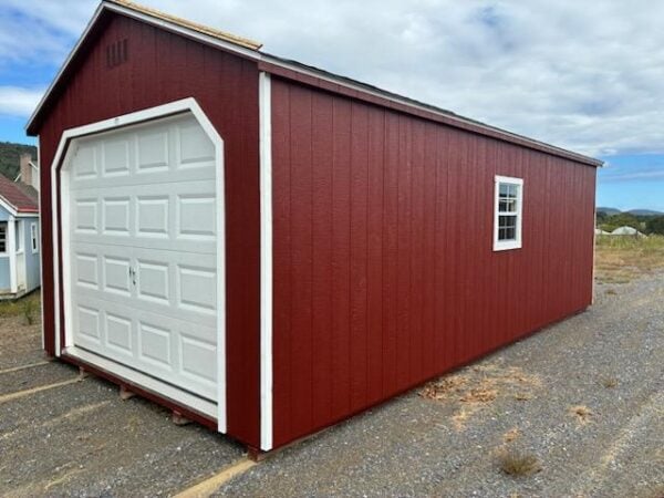 Red A-frame garage with white overhead door, black and white trim, single side entry door, and two windows with white trim, featuring a 4-foot interior loft.