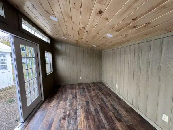 Interior of a modern leantoo office shed with pine ceiling, wood-look laminate flooring, insulated windows, and recessed lighting.