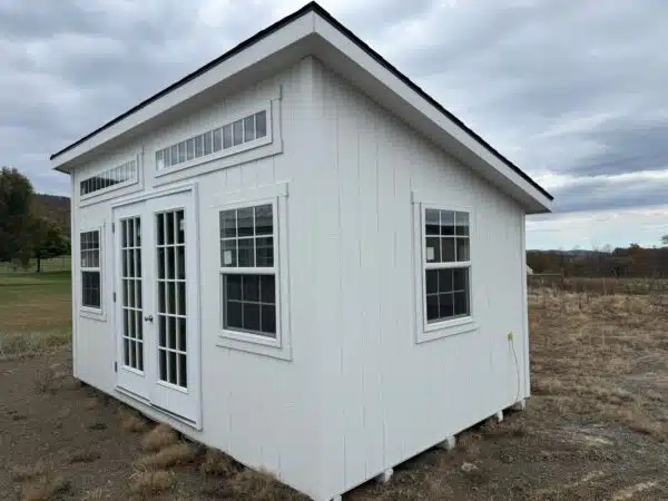 White leantoo office shed with double glass doors, transom windows, and large insulated windows, set on a gravel lot under a cloudy sky.