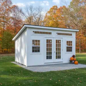 White modern leantoo office shed with double glass doors and transom windows, set on a gravel pad with fall foliage in the background.