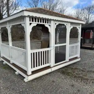 Angled exterior view of a 12x12 white vinyl deluxe gazebo showing the screened entry door, square spindle railing, Shakewood shingles, and saddle Trex floor