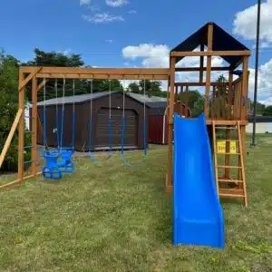 Climber swing set with 5-foot square tower, rock wall with blue climbing holds, blue slide, and multiple swings.